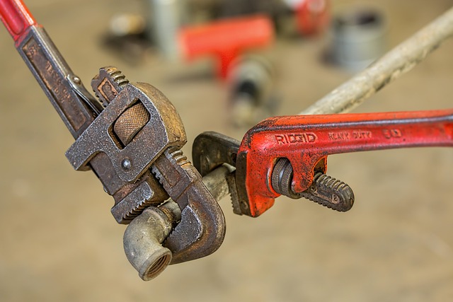 Two pipe wrenches gripping a metal pipe fitting