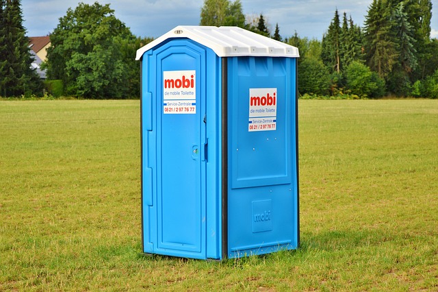 A blue portable toilet in a grassy field