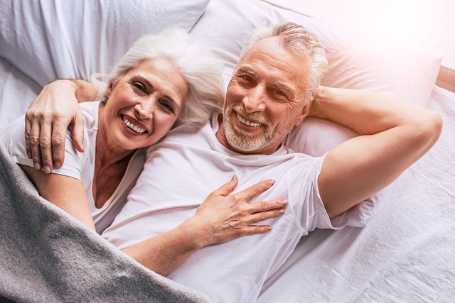 An elderly couple smiling while lying in bed together