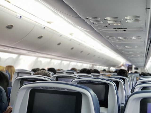 An airplane cabin interior with seatback screens and seated passengers