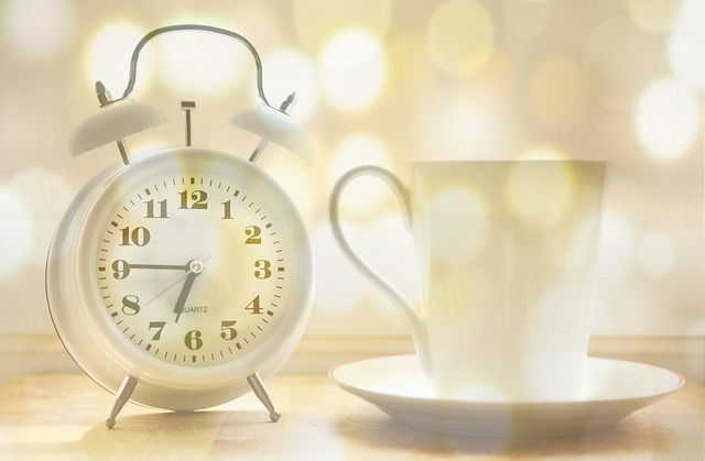 A white alarm clock next to a coffee cup on a table