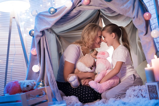 A mother and daughter smiling inside a cozy indoor blanket fort