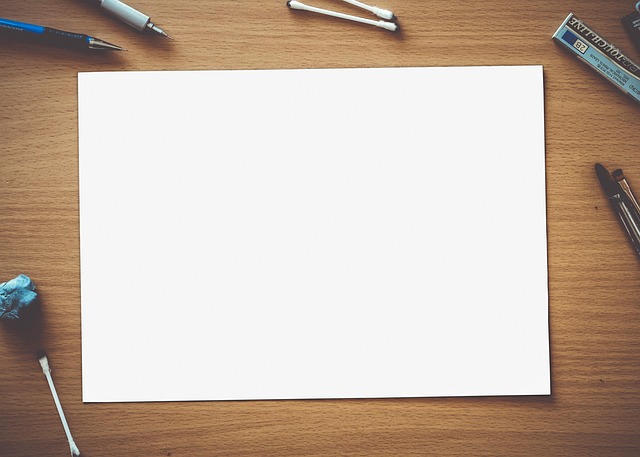 A blank sheet of white paper surrounded by stationery on a desk